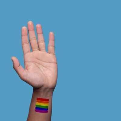 Cropped photo of an adult man lifting up the hand with the rainbow flag pattern on the wrist